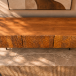 Elevated view of the Lunar Spec bar cabinet, showing a wide top with visible wood grain, three textured doors in a warm brown finish and slim dark legs.
