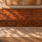 Elevated view of the Porticco bar cabinet in a warm brown wood finish, showing a wide grained top, doors with square and rectangular panel detailing, dark handles and exposed hinges.