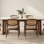 Front view of the OREN dining table with an ivory rectangular top, brown wood finish supports and gold accents, surrounded by six chairs with woven cane backs and beige upholstered seats.