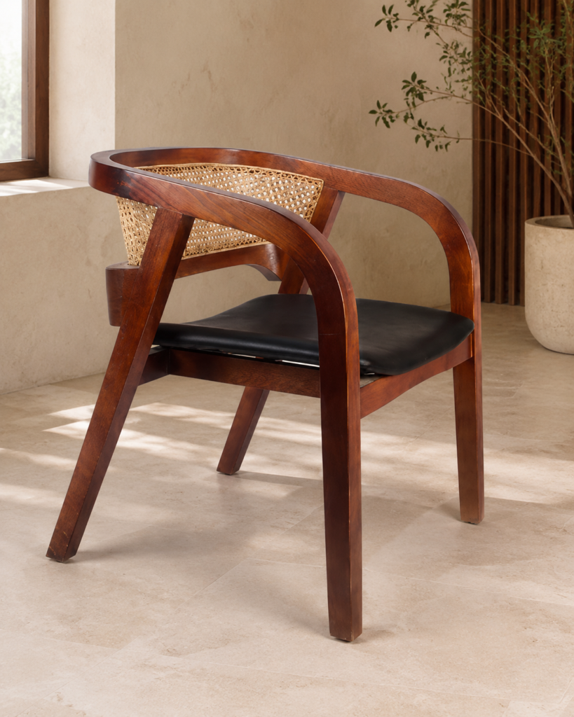 Angled side view of the CAFFEINA chair with a warm-finished acacia wood frame, curved arms, natural cane backrest and black upholstered seat.