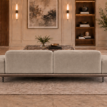 Rear view of the Continentale sofa in light beige Aston 924 upholstery, with two broad back panels, low padded arms, a brown base and slim dark legs.