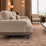 Side view of the Continentale sofa in light beige upholstery, with a broad padded arm, deep seat, angled back cushions and a brown base on slim dark legs.