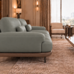 Side view of the Continentale sofa in grey-green Phantom 124 leatherette, showing a broad padded arm, angled back cushions, a teak finish base and slim dark legs.