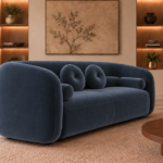 Angled side view of the Formosa sofa upholstered in deep blue Giza 114 fabric, showing its continuous curved back, rounded arms and matching cushions.