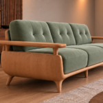 Angled side view of the Grand Turismo sofa in sage green Aston 922 fabric, with a curved wooden side panel, raised armrests, stitched back cushions and tapered legs.