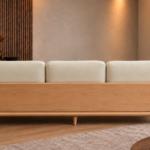 Rear view of the Grand Turismo sofa with three ivory Aston 902 fabric back cushions, a broad light wood rear panel, rounded armrests, curved frame and tapered legs.