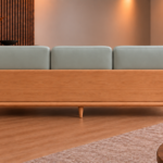 Rear view of the Grand Turismo sofa with three light grey-green Phantom 117 leatherette back cushions, a broad wooden back panel, rounded armrests and tapered legs in a light teak finish.