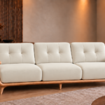 Front view of the Grand Turismo three-seater sofa in ivory Phantom 102 leatherette, featuring stitched back cushions, broad wooden armrests, curved side panels and a light wood frame with tapered legs.