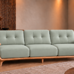 Front view of the Grand Turismo three-seater sofa in light grey-green Phantom 117 leatherette, with stitched back cushions, broad wooden armrests, curved side panels and a rounded base on tapered legs.
