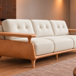 Angled side view of the Grand Turismo sofa in ivory Phantom 102 leatherette, showing a curved wooden side panel, raised armrest, stitched back cushions and tapered legs beneath a rounded base.