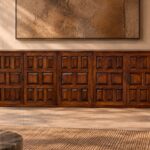 Front view of the Porticco bar cabinet in a warm brown wood finish, featuring five panelled doors, repeating square and rectangular details, dark decorative handles, exposed hinges and a low base.