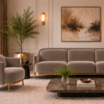 Front view of the Duet three-seater sofa and matching armchair in taupe patterned Aston 925 upholstery, with rounded arms, individual seat and back cushions, gold finish base trim and slender legs.