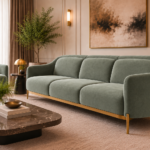 Angled side view of the Duet three-seater sofa in sage green patterned Aston 922 upholstery, showing curved arms, three separate cushions, gold finish base trim and slender legs, with a matching armchair nearby.