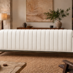 Rear view of the Venetia sofa in white leatherette, featuring vertical channels across the full back, rounded upholstered arms, a dark rail with gold trim and gold-finish metal supports.