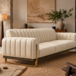 Angled side view of the Venetia sofa in cream leatherette, showing vertical channels across the backrest and outer arm, three seat cushions, dark base trim and gold-finish sled supports.