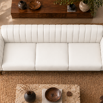 Overhead view of the Venetia sofa in white leatherette, showing three equal seat cushions, vertical channels along the backrest, rounded channelled arms and gold-finish supports at the front corners.