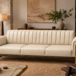 Front view of the Venetia three-seater sofa in cream leatherette, featuring three seat cushions, a vertically channelled backrest, rounded upholstered arms and gold-finish metal supports extending up the arm fronts.