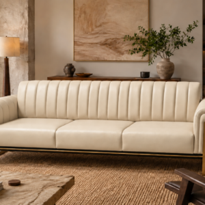 Front view of the Venetia three-seater sofa in cream leatherette, featuring three seat cushions, a vertically channelled backrest, rounded upholstered arms and gold-finish metal supports extending up the arm fronts.