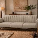 Front view of the Venetia sofa in light taupe leatherette, featuring three seat cushions, a vertically channelled backrest, rounded upholstered arms and gold-finish supports beside a dark base rail.