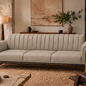 Front view of the Venetia sofa in light taupe leatherette, featuring three seat cushions, a vertically channelled backrest, rounded upholstered arms and gold-finish supports beside a dark base rail.