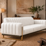 Angled side view of the Venetia sofa in white leatherette, showing its rounded channelled arms, vertically stitched backrest, three seat cushions and gold-finish sled supports beneath a dark base rail.