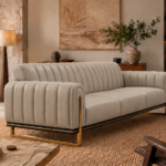 Angled side view of the Venetia sofa in light taupe leatherette, showing channelled upholstery across the back and rounded arms, three seat cushions and gold-finish sled supports.